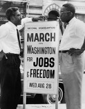 Bayard Rustin (left) speaking with person holding a sign advertising the 1963 March on Washington for Jobs and Freedom