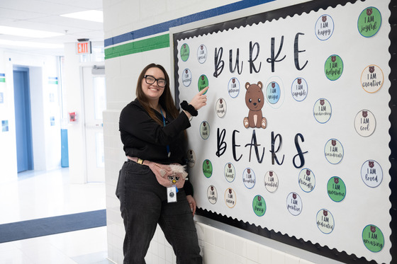 teacher smiles and points at a bulletin board
