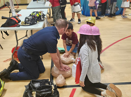 A paramedic showing 4 elementary students how to perform CPR on practice pillow.