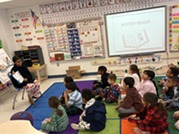 Sixth grader reading to class of 1st graders.