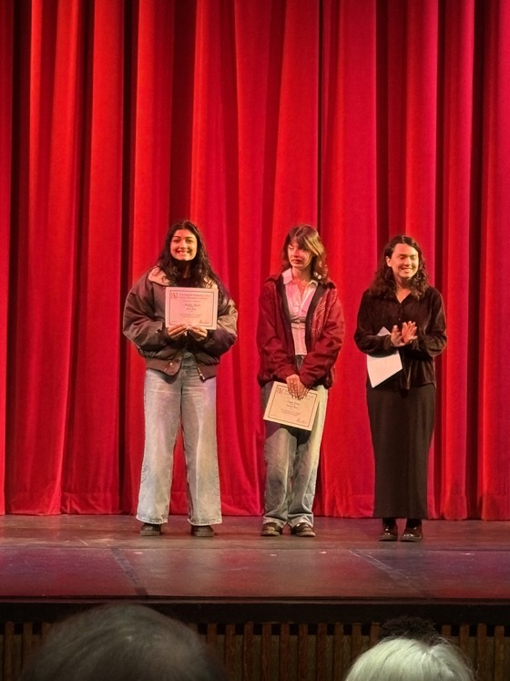 High school students hold certificates on a stage with red curtains at an ESU Shakespeare competition