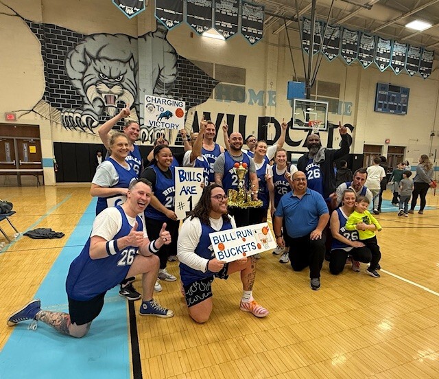 staff basketball team holding a trophy in the middle of a gym