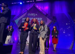 three students posing in front of DECA logo