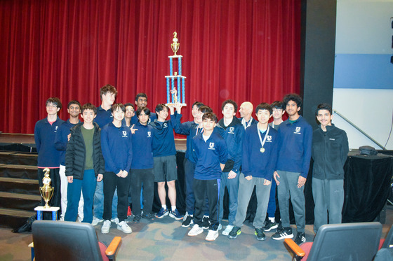 The entire TJ chess team holds up the major level tournament championship trophy in auditorium.