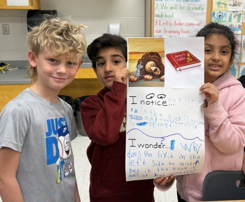 3 first grade students holding a large paper upon which they have written what they notice and what they wonder about a picture.