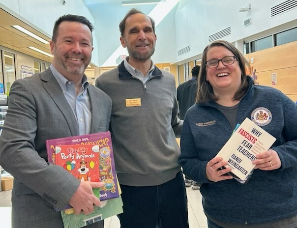 Three adults standing together holding books