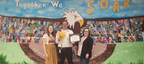 teachers smile for a photo in front of their school mural with an award