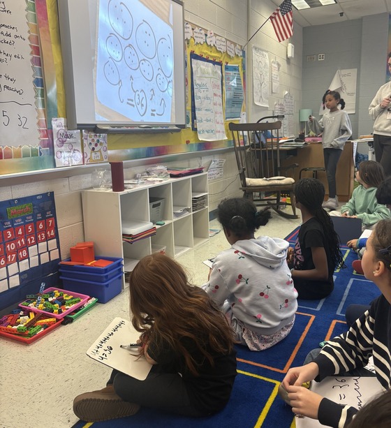 Students working out multiplication problems on the smartboard and whiteboards