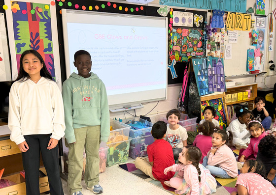 A boy and a girl standing in front of a group of students 