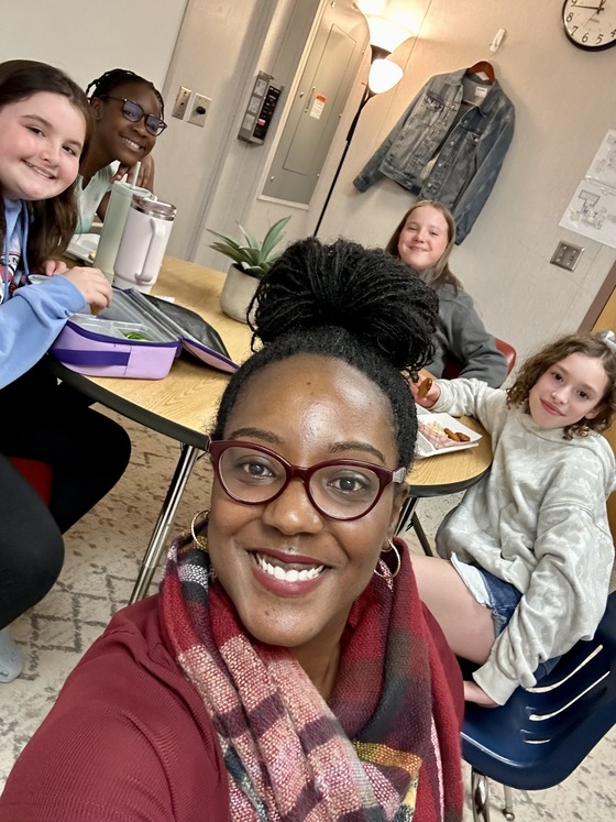 Four 5th grade girls and assistant principal having lunch around an oval table.  It is called a lunch bunch.