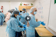 Picture of students putting on gowns with video play button overlayed