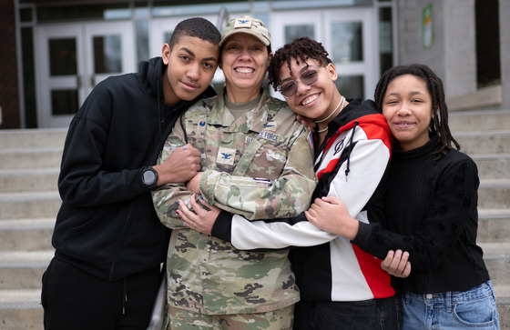 A mom in a space force uniform is hugged by three kids