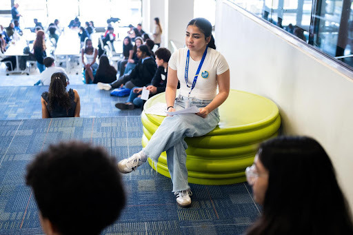 A girl sits on a stool listening to other students