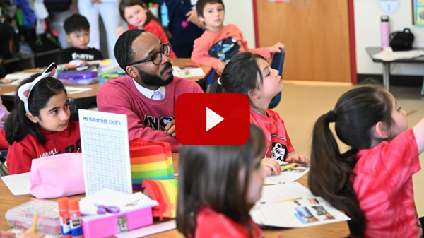 Screenshot of an adult sitting among young kids in a class