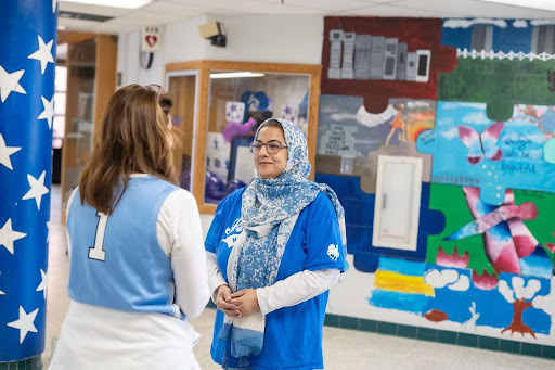 Two adult females talk in a school hallway