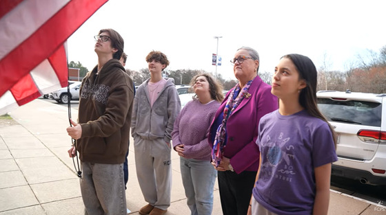 Dr. Reid and a group of students watch as another student raises the American Flag outside
