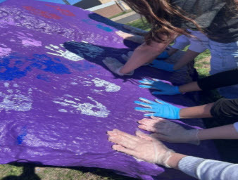 purple rock with hands placing painted handprints