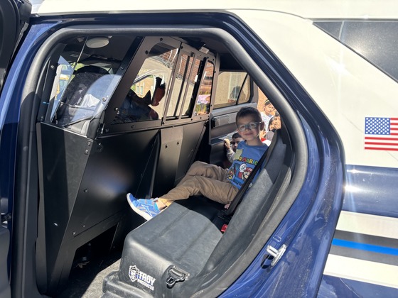 A student sits in the back of a police car during career day 