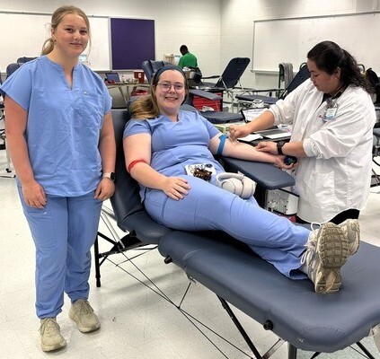 Student standing beside seated student having blood drawn