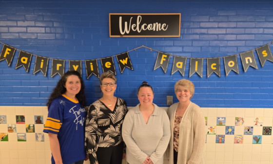 4 woman standing in front of a "Fairview Falcons" banner smiling