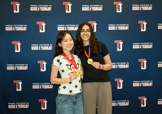 A couple of the National Merit Semifinalists pose with their medals in front of a TJ logo backdrop