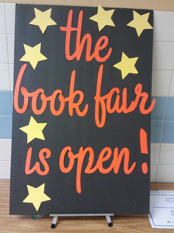 Sign with black background and bright yellow stars with text "The Book Fair is Open."