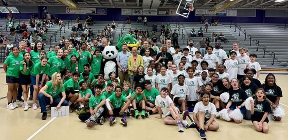A large group of Greenbriar students, staff, and mascots wearing "One Greenbriar" shirts pose together on a gymnasium floor.