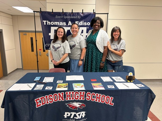 Group of women standing in front of high school PTSA table during an event