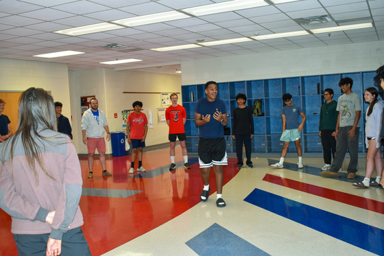 Students standing in a circle. One student is in the middle showing exaggerated expression as part of the workshop.