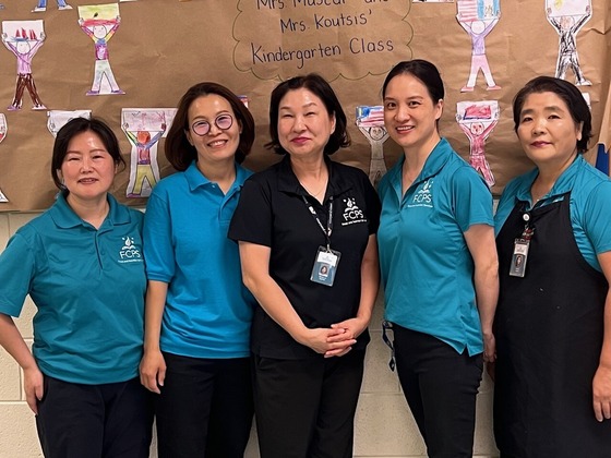 Five cafeteria staff members posed in front of children's drawings