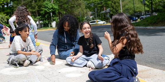 Girls laugh while coloring with chalk on a sidewalk