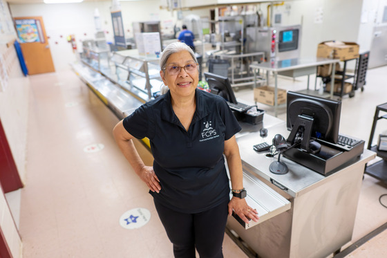 A food services worker stands in a school cafeteria smiling