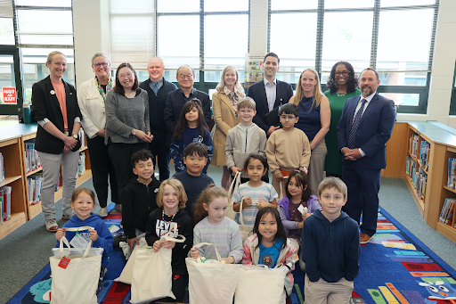 Group photo in a library with students in the foreground holding tote bags
