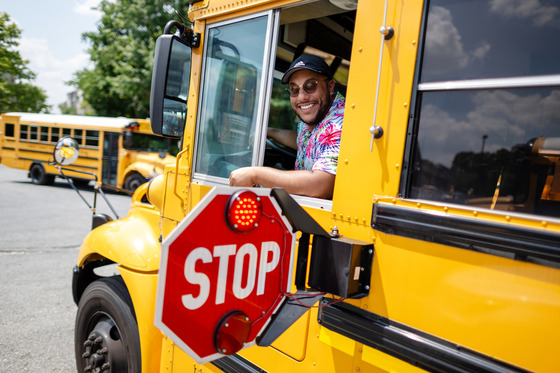 A smiling bus driver looks out his bus window. 