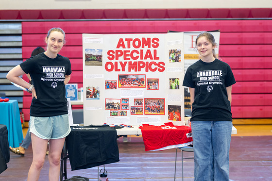 Students stand at an exhibit table in a school gym. 