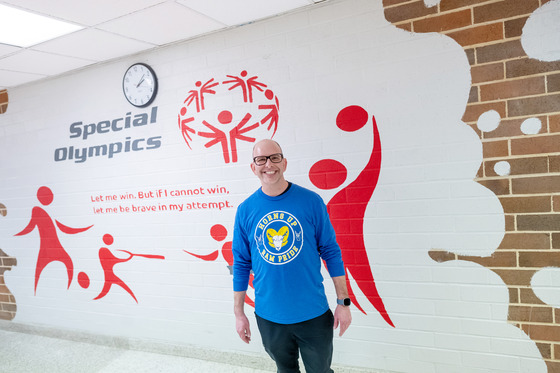 A teacher stands in front of a Special Olympics mural 