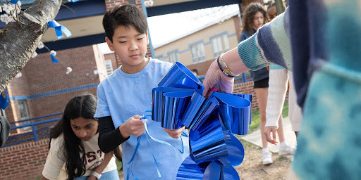 And adult hands a blue ribbon to a boy under a tree. 
