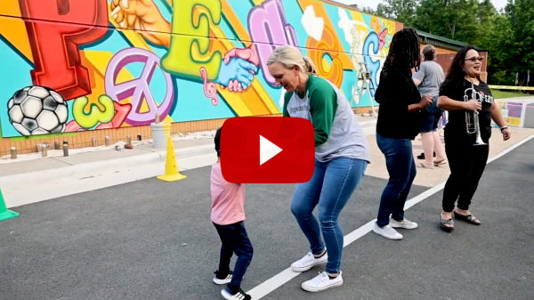Screen shot with teacher dancing with a student in front of an outdoor mural