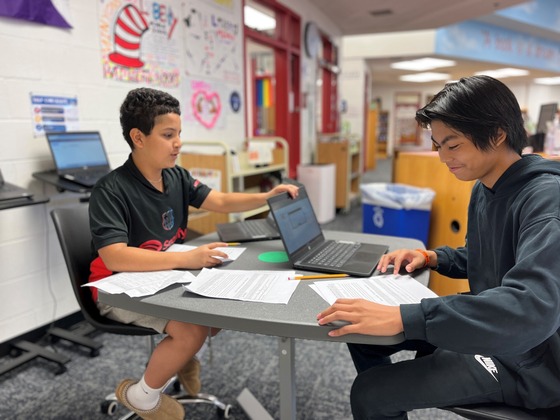 Two students interviewing each other with laptops in the library