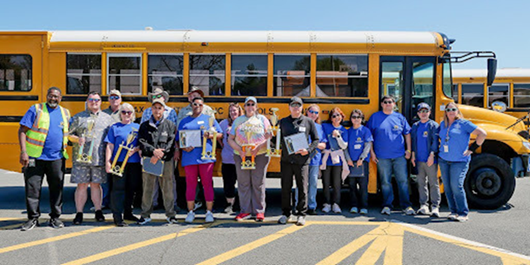 Bus Drivers in front of a bus holding a trophy 