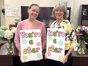 two women holding cards that say You're a Star in an office with flowers in a vase on the desk