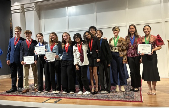 Students on stage wearing medals and holding up certificates 