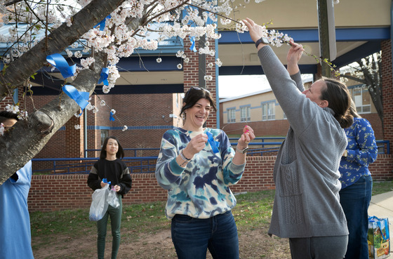 Staff member smiling while tying blue ribbons to a tree