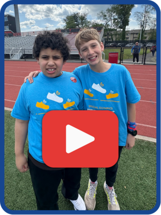 Two students smiling , standing on a track, with a play button in the middle of the image