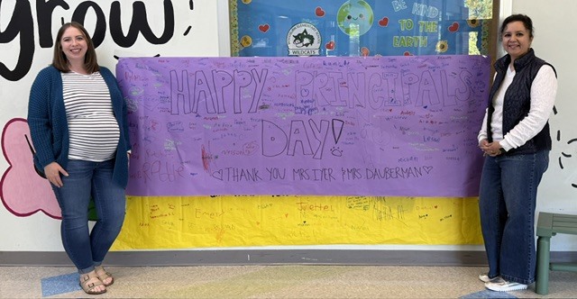 Ms. Dauberman and Ms. Iyer stand by a purple banner 