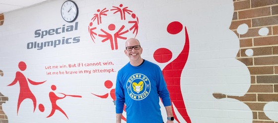 Paul Arena smiling in front of Special Olympics mural