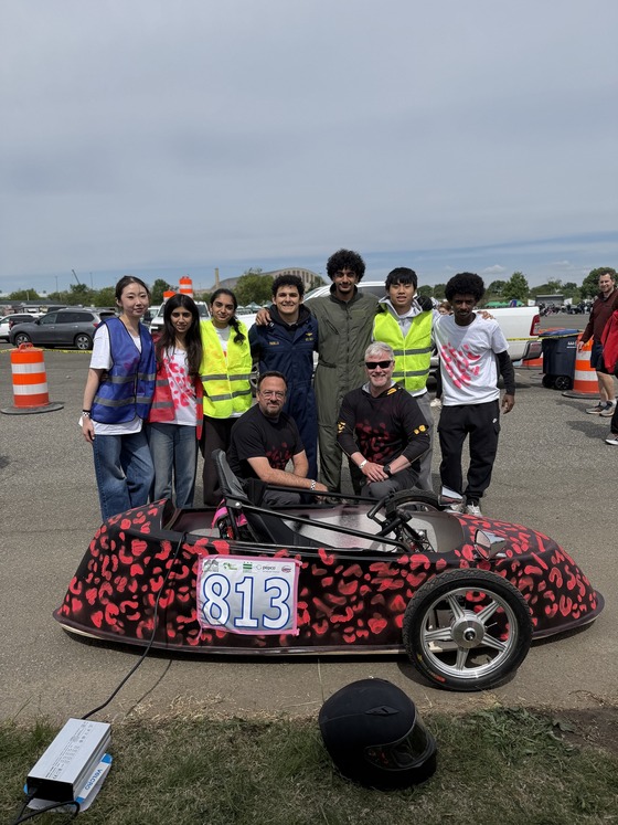 The entire TJ Electric Vehicle Grad Prix Team posing behind their electric vehicle on the racetrack.