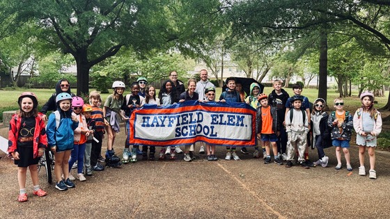 Students and staff lined up with a school sign for Bike and Roll to School at Hayfield Park
