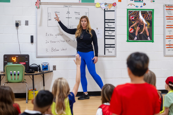 A gym teacher points to a drawing on a white board