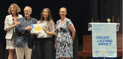 Student on stage holding certificate while standing beside adults